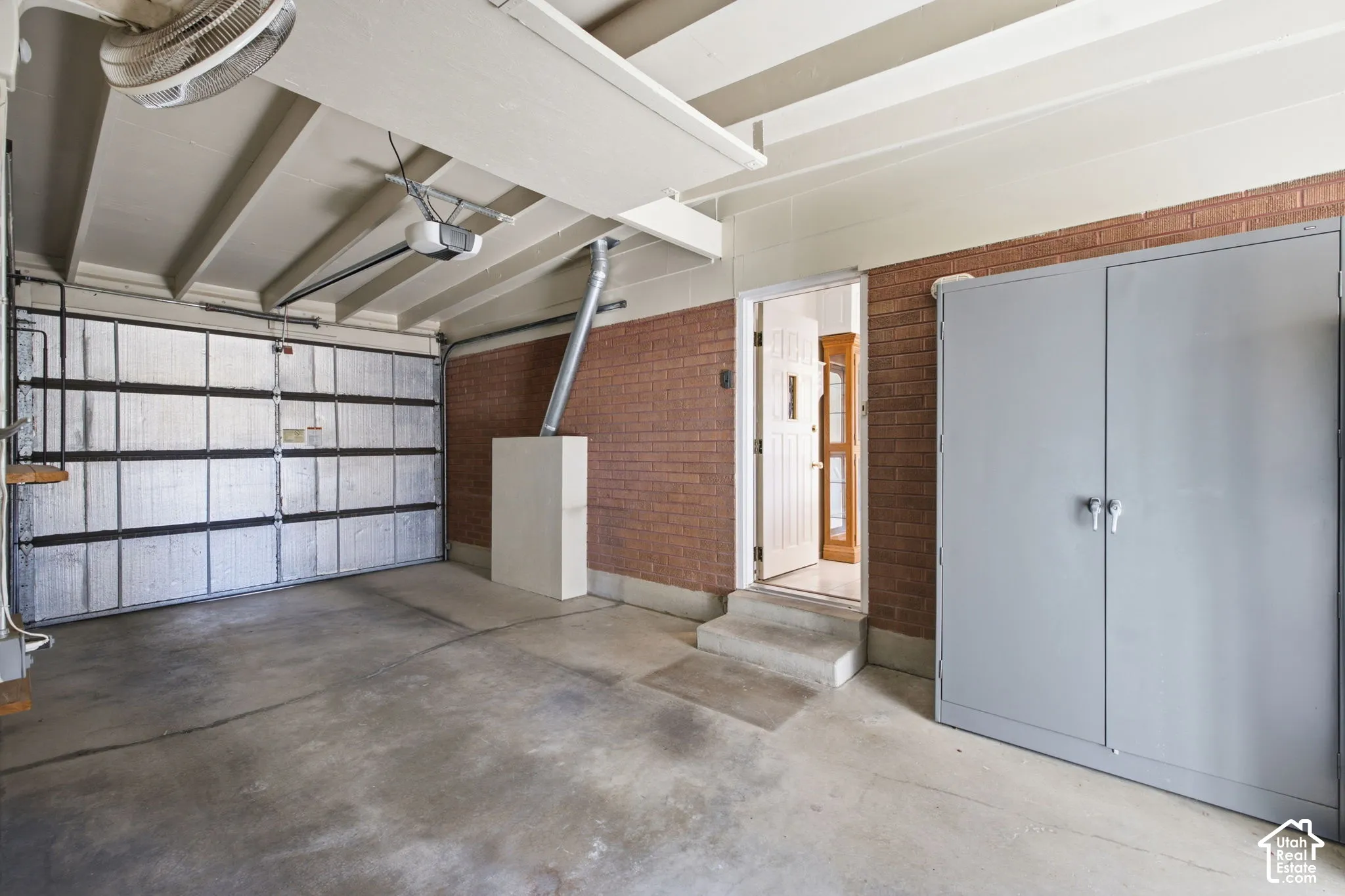 Concrete flooring garage with an automatic garage door opener, brick wall accents, and an integrated storage cabinet