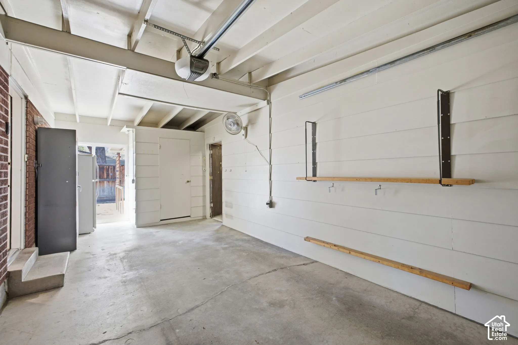 Concrete flooring, exposed ceiling beams, built-in wall shelving, and an automatic garage door opener