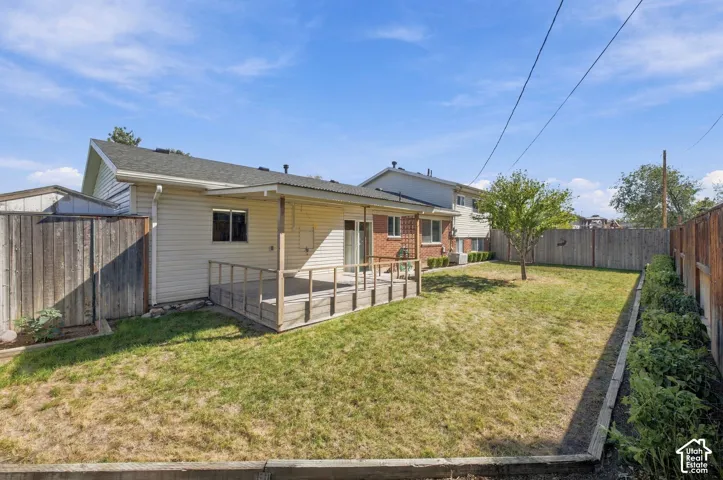 Expansive backyard featuring a wood deck, mature tree, established garden bed, and wood fencing