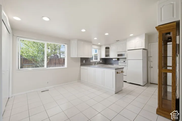 White cabinetry, light-toned tile flooring, recessed ceiling lighting, a kitchen island, and a large window