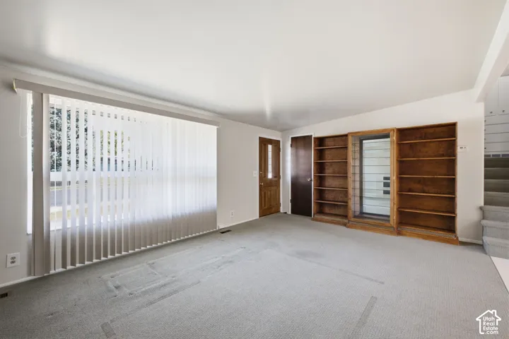 Expansive window with vertical blinds, built-in wooden shelving, and a wood-paneled door