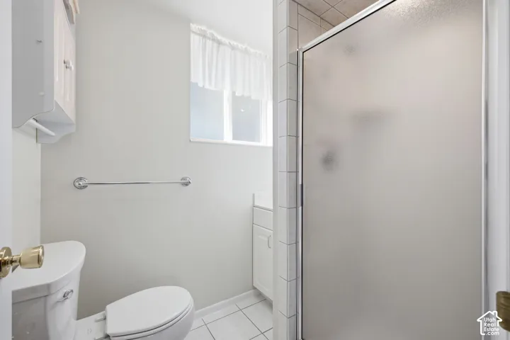 Enclosed shower with frosted glass, white tiled flooring, and a window for natural light