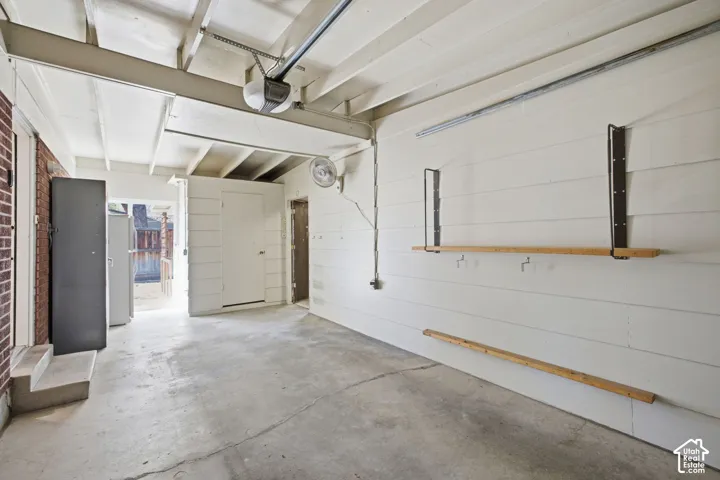 Concrete flooring, exposed ceiling beams, built-in wall shelving, and an automatic garage door opener