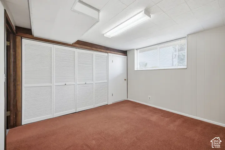Textured acoustic ceiling tiles with fluorescent lighting, louvered bi-fold closet doors, wood paneling, and a single window with blinds