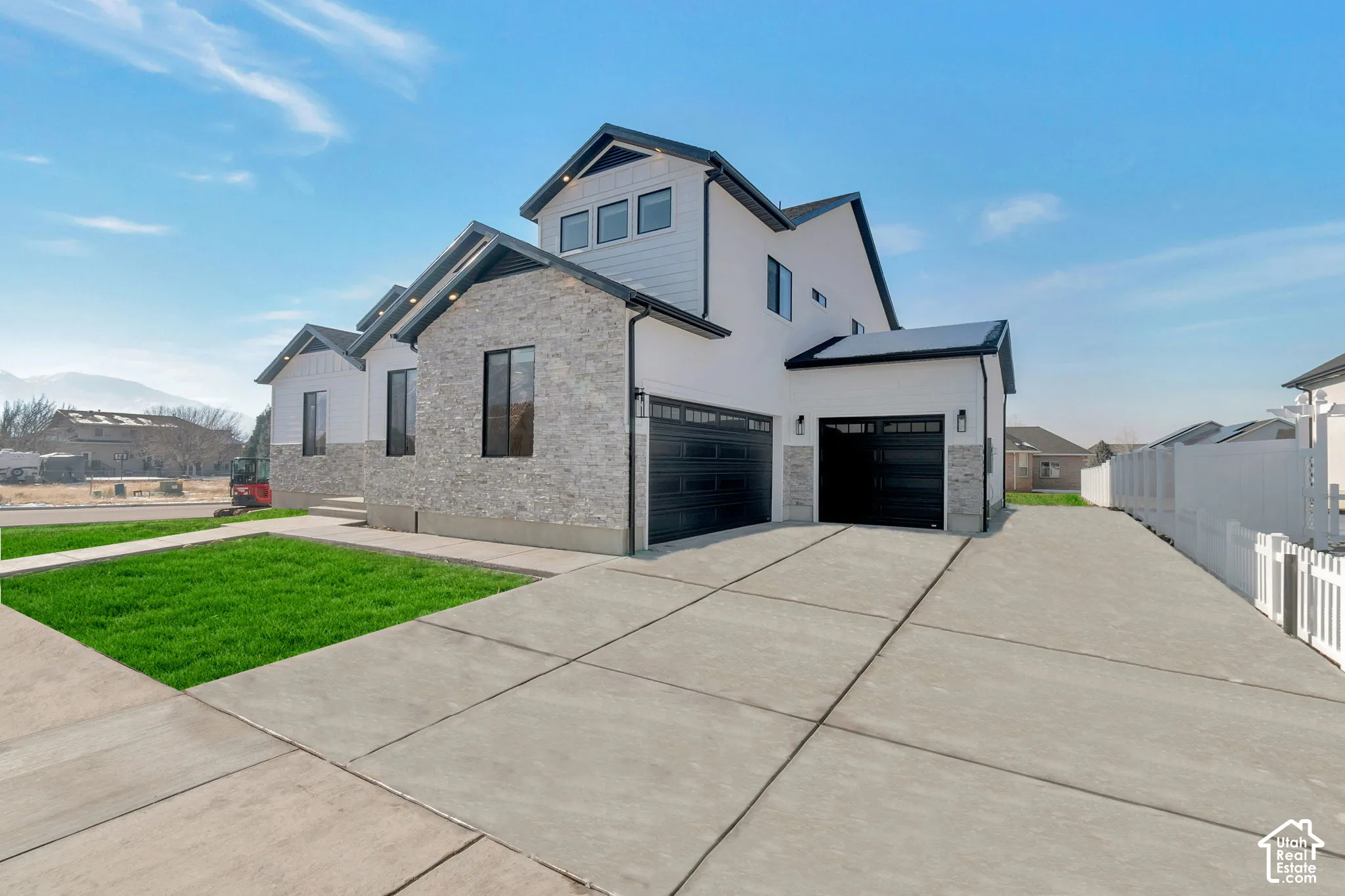 Modern exterior featuring stone veneer and white siding, a concrete driveway, and multiple garage doors