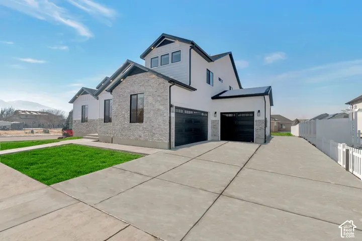 Modern exterior featuring stone veneer and white siding, a concrete driveway, and multiple garage doors
