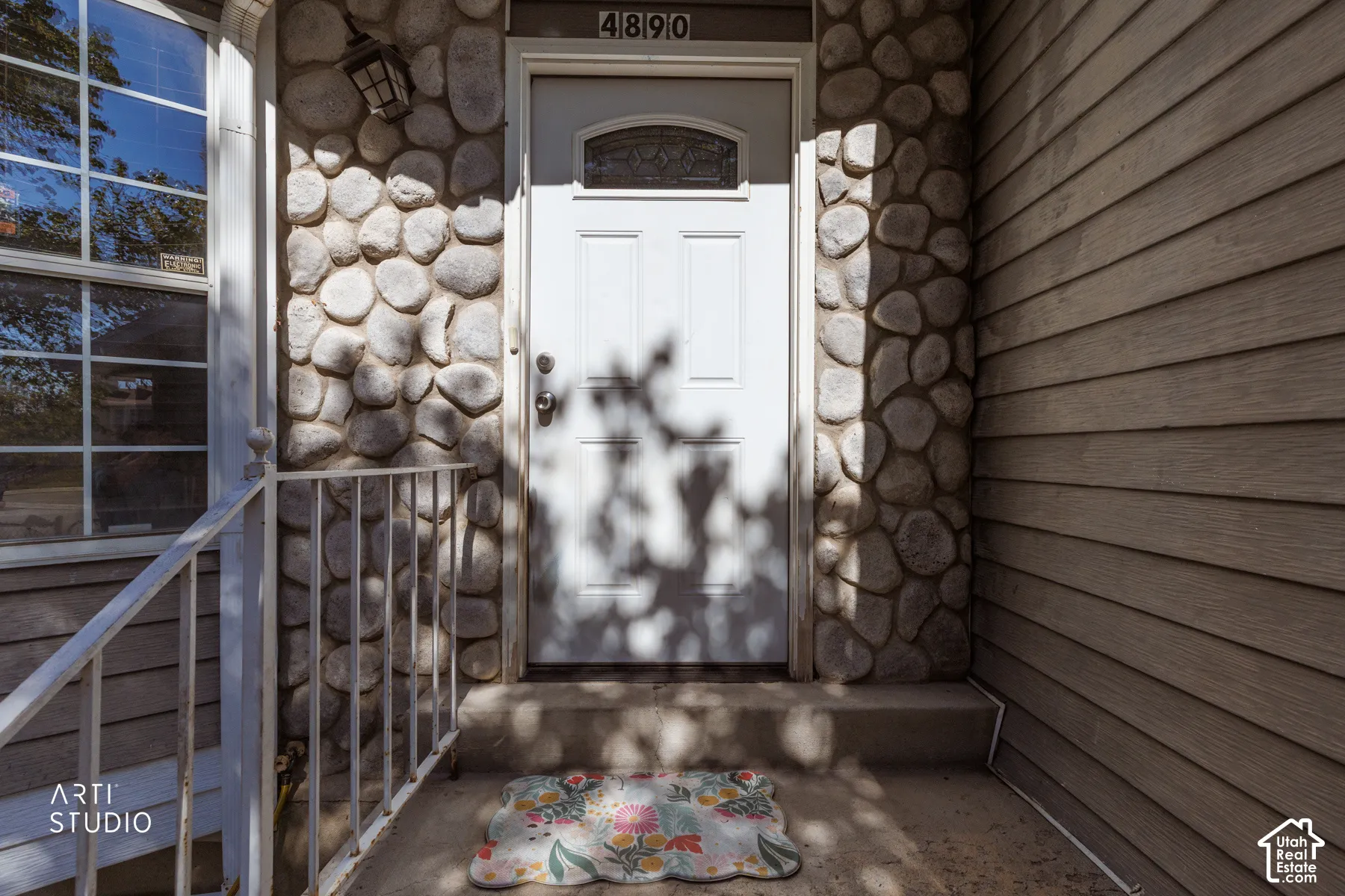 Stone veneer facade with horizontal siding accents, white entry door with decorative glass, and a metal handrail