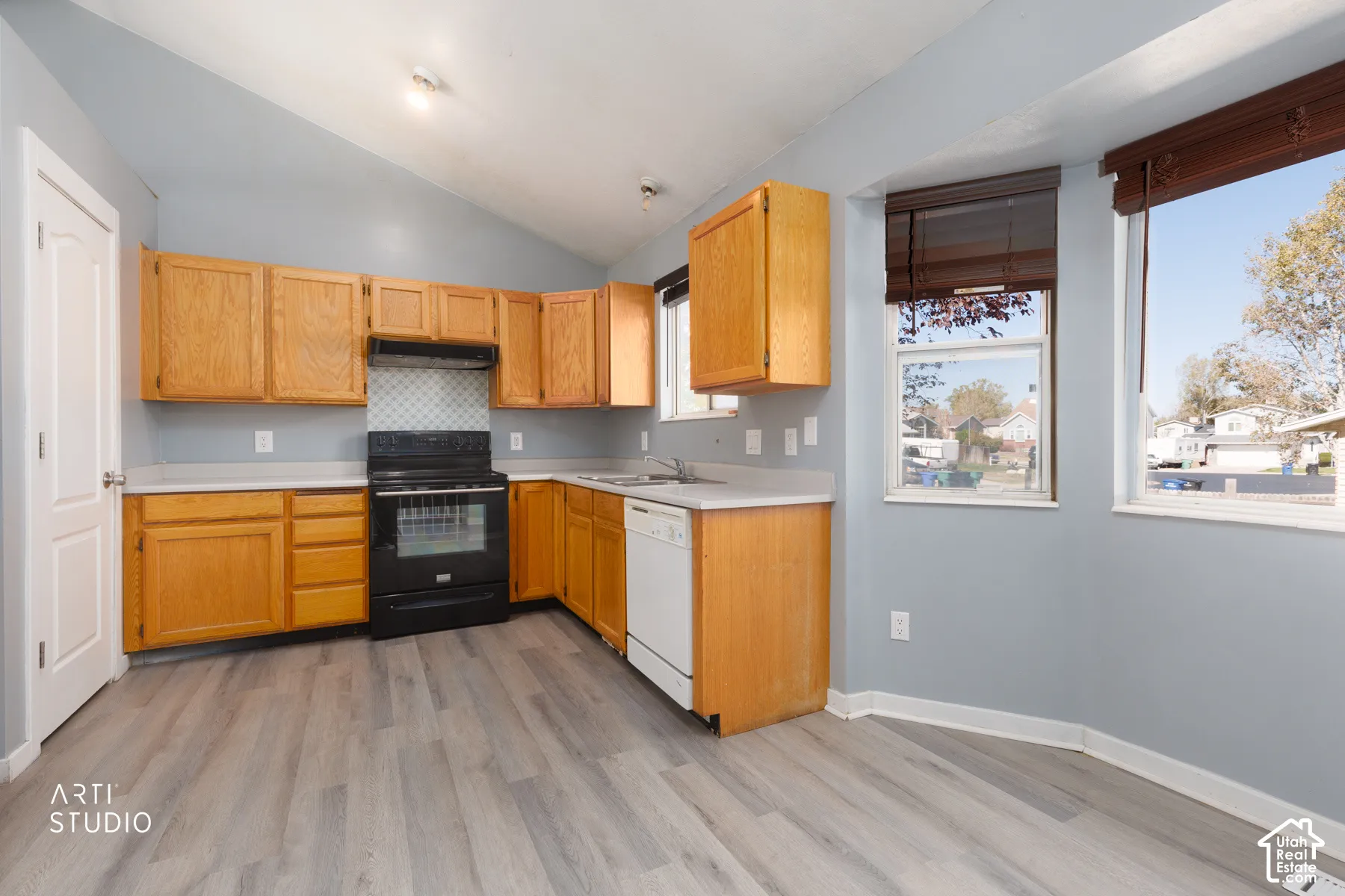 Kitchen with wood-finish flooring, vaulted ceiling, wood cabinetry, built-in black range, and dual windows