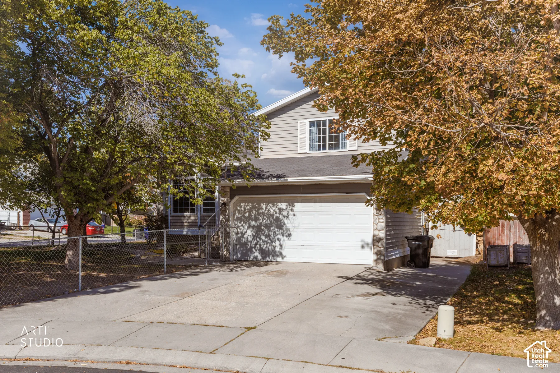 Two-story residence featuring horizontal siding, an attached garage, a paved driveway, and mature trees