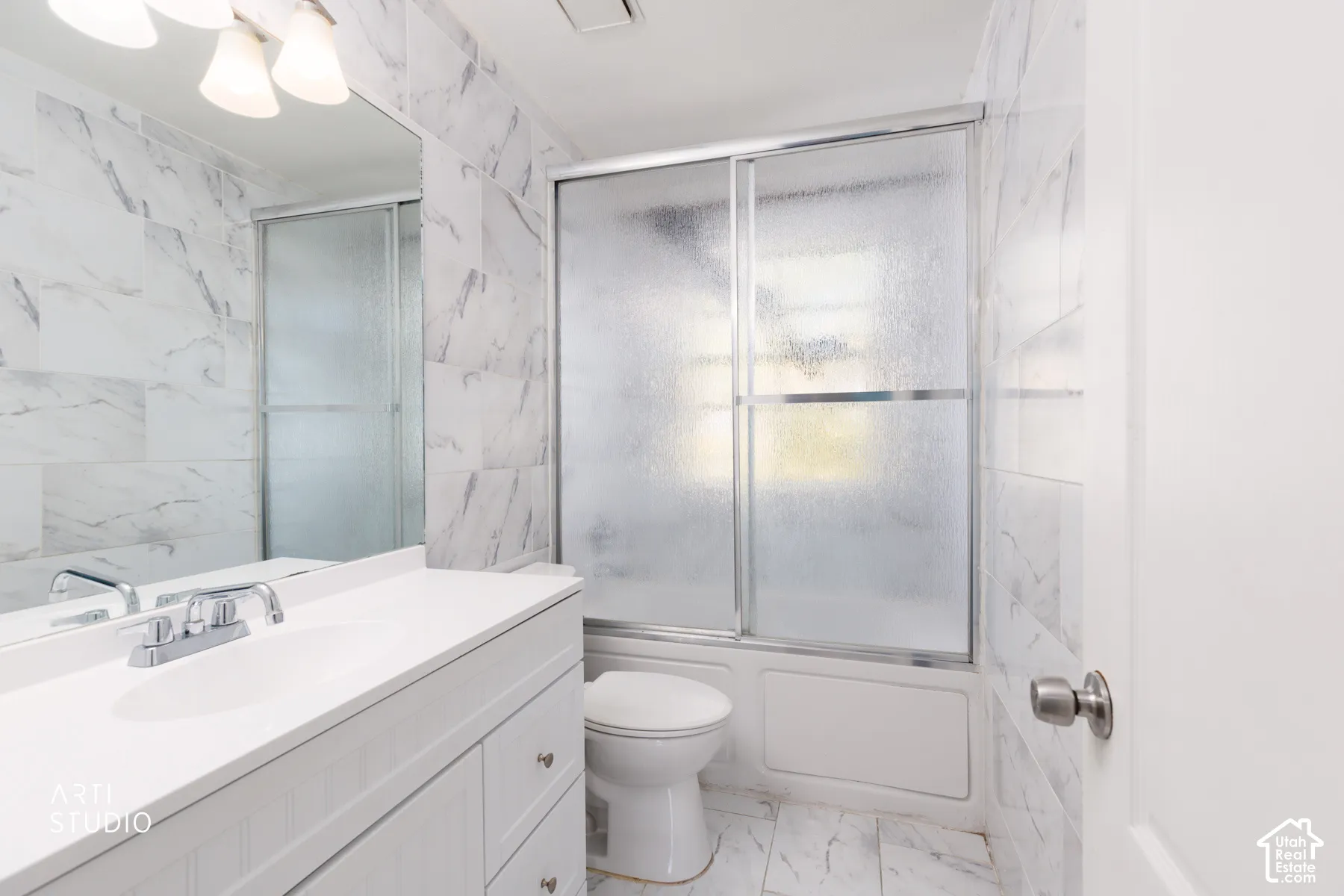 White vanity with chrome faucet and undermount sink, large mirror, and tiled walls with a white-finish tub and sliding glass shower door