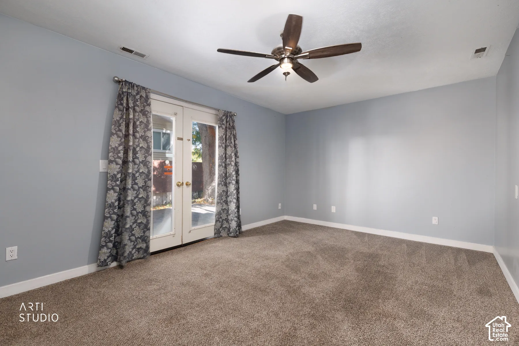 Light blue wall finishes with white trim, brown carpet, ceiling fan, and double French doors with glass panels