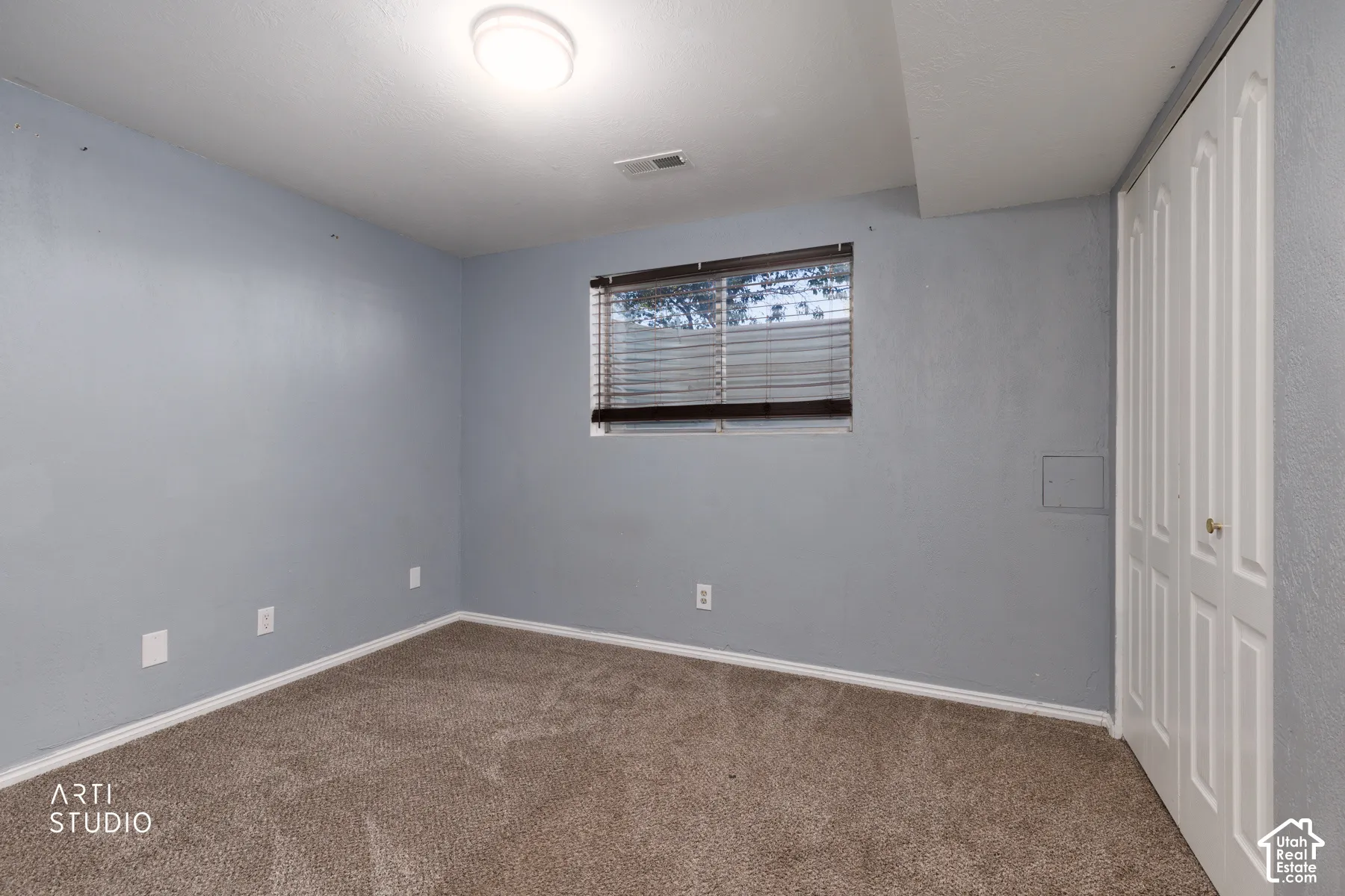 Carpeted room with light blue walls, a ceiling-mounted light fixture, and a window with horizontal blinds