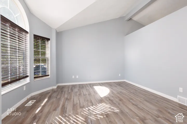 Vaulted ceilings, wood-finish flooring, and multiple windows with blinds