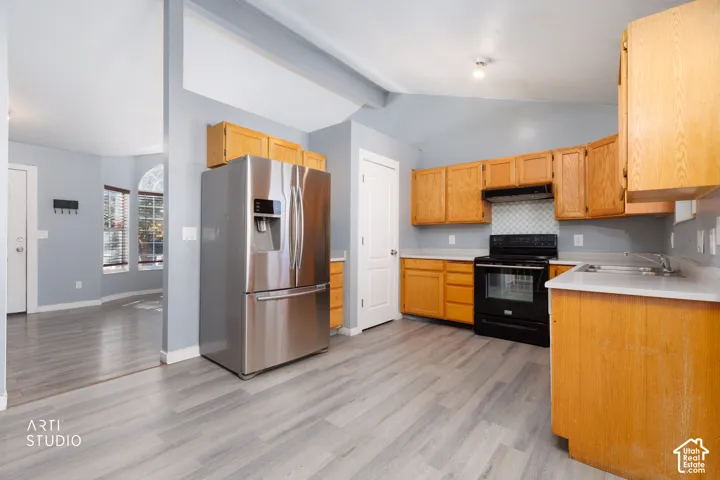 Kitchen featuring wood-finish flooring, stainless steel refrigerator, black range, wood cabinetry, and light-toned countertops