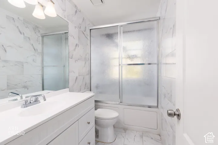 White vanity with chrome faucet and undermount sink, large mirror, and tiled walls with a white-finish tub and sliding glass shower door