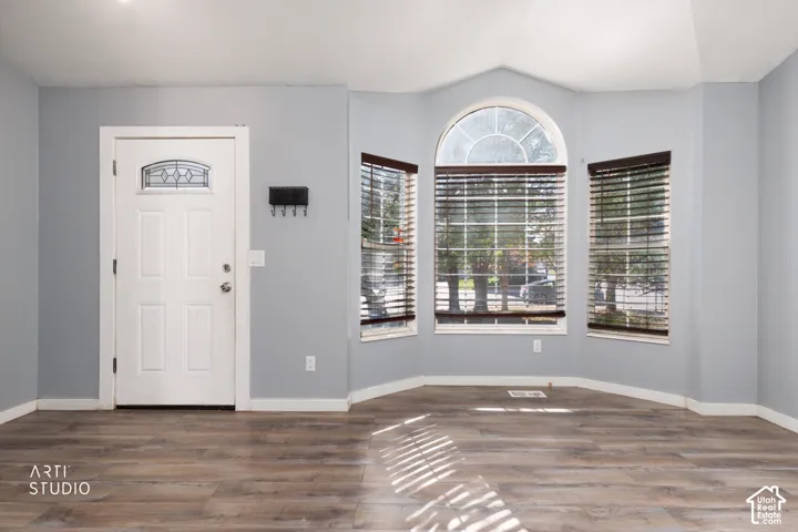 Wood-finish flooring throughout, bay windows with blinds, arched transom window, and a paneled entry door with decorative glass insert