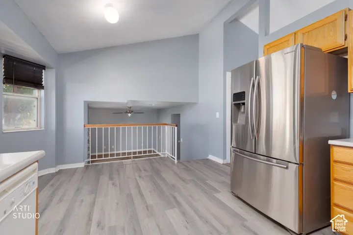 Wood-finish flooring, vaulted ceiling, stainless steel refrigerator, white railing, and light wood cabinetry