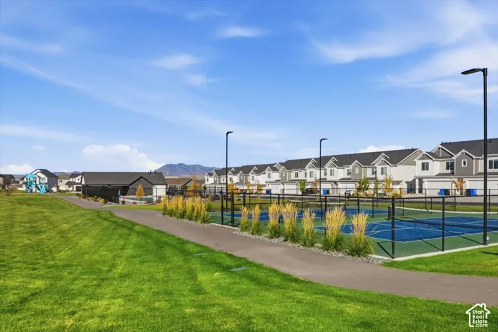 Expansive green space and paved pathway alongside a fenced tennis court