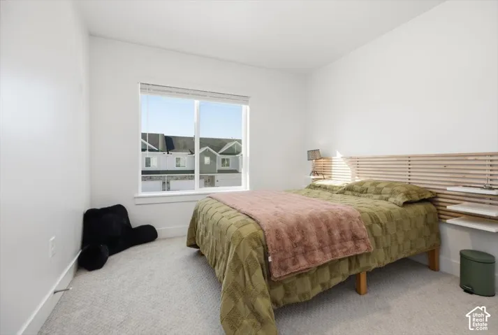 Bright bedroom featuring a large window, light-colored walls, and neutral carpeting