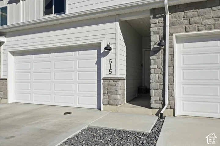 White paneled garage door, stone veneer accents, and exterior wall sconces