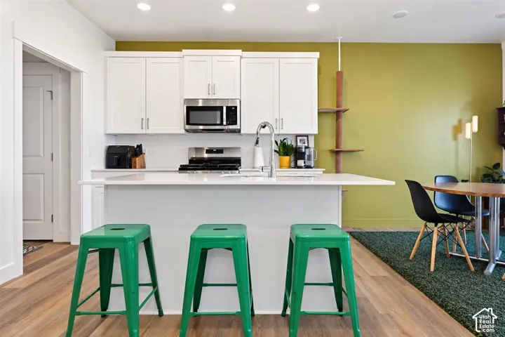 Contemporary kitchen featuring white cabinetry, stainless steel appliances, a white countertop, and wood-finish flooring