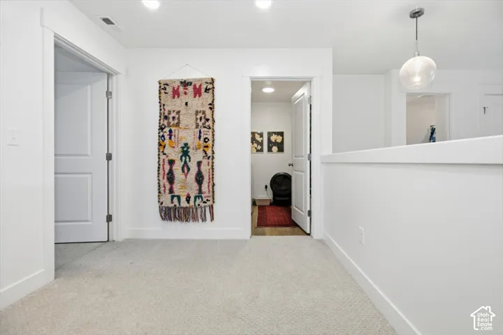White interior walls, light-toned carpet, recessed ceiling lighting, two-panel interior doors, light wood-finish flooring visible in doorway