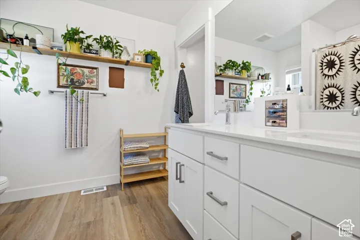 White dual vanity with integrated sinks, chrome fixtures, a large wall-mounted mirror, white shaker cabinetry, and wood-finish flooring