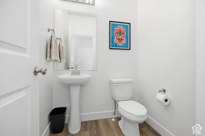 White pedestal sink, chrome faucet, wall-mounted mirror, white toilet, and wood-finish flooring