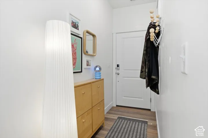 Wood-finish flooring with crisp white walls, a light wood shoe cabinet, and a white paneled door