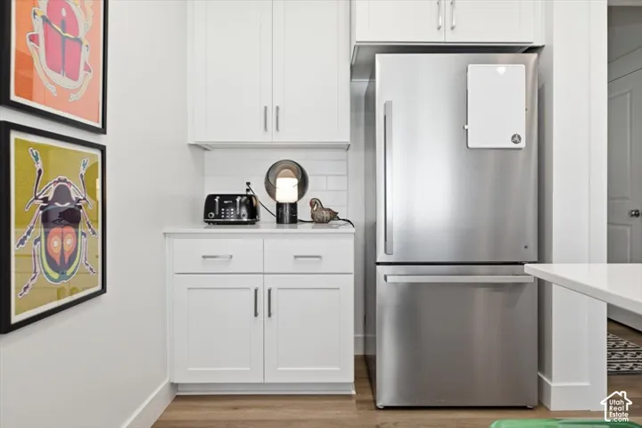 Stainless steel refrigerator with bottom freezer, white shaker-style cabinetry, white subway tile backsplash, and wood-finish flooring