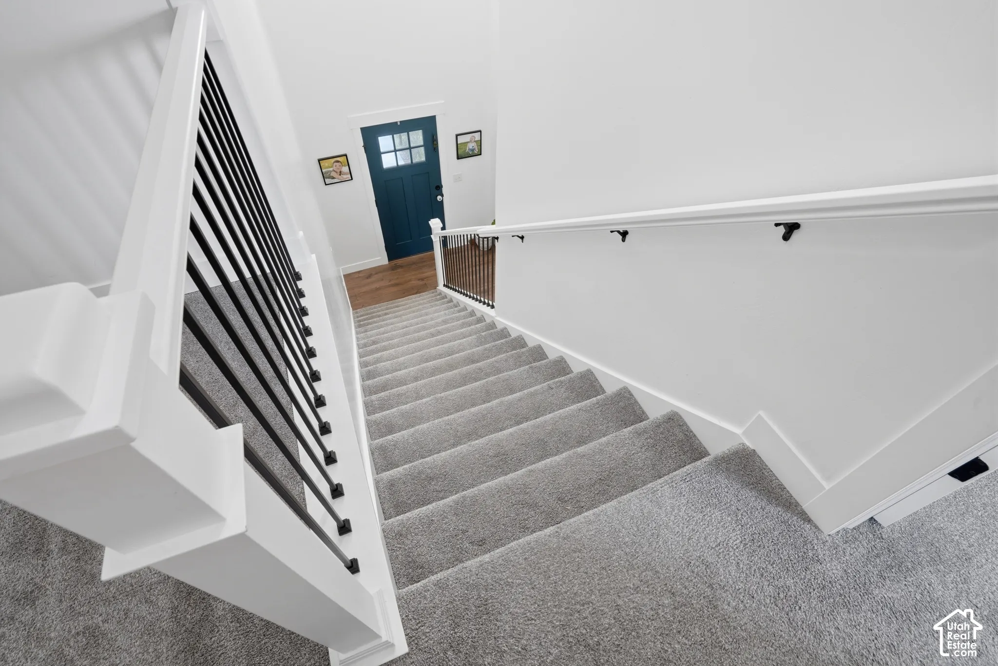 Carpeted staircase featuring a modern black metal spindle railing and a white handrail