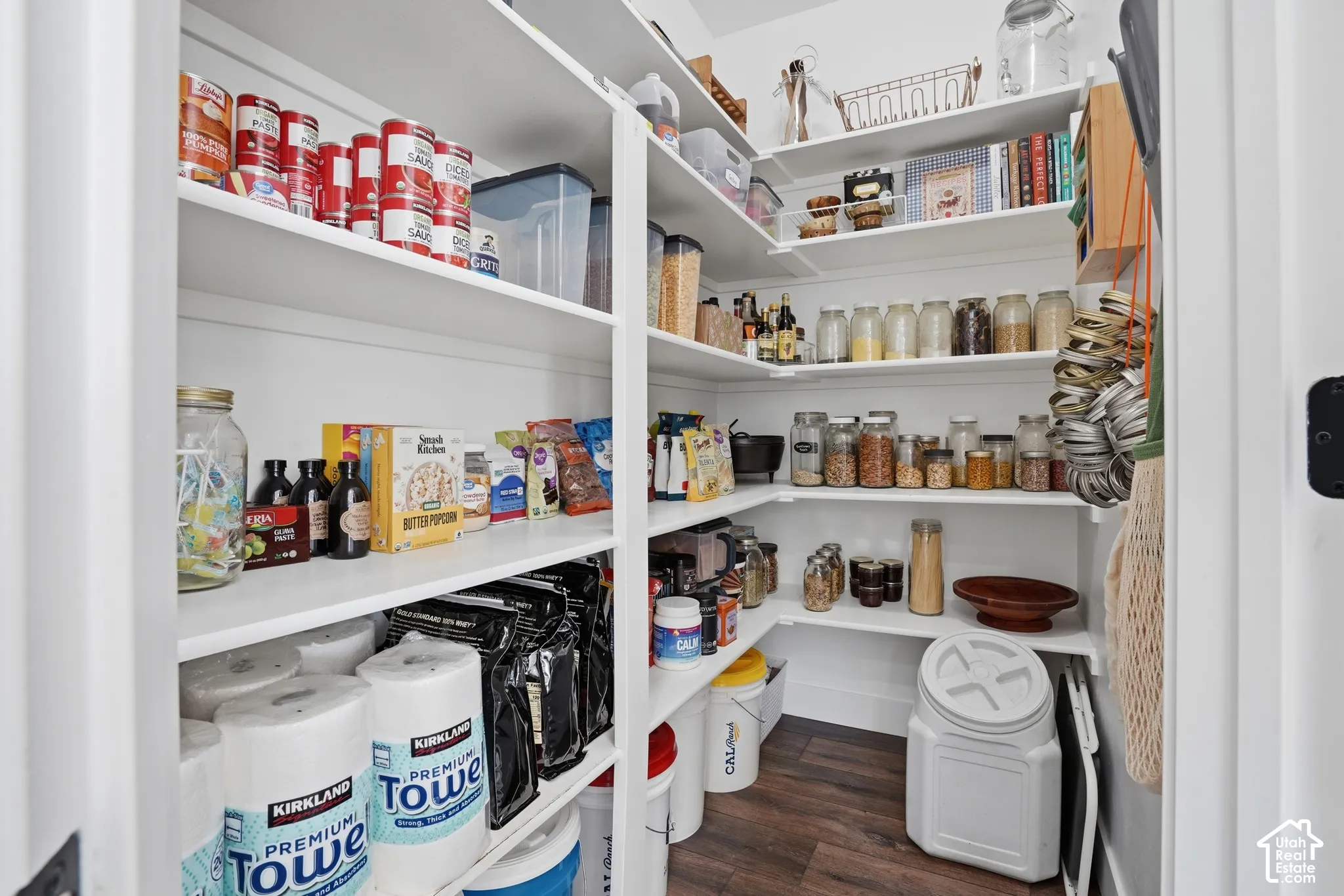 Walk-in pantry featuring white shelving, wood-finish flooring, and ample storage space