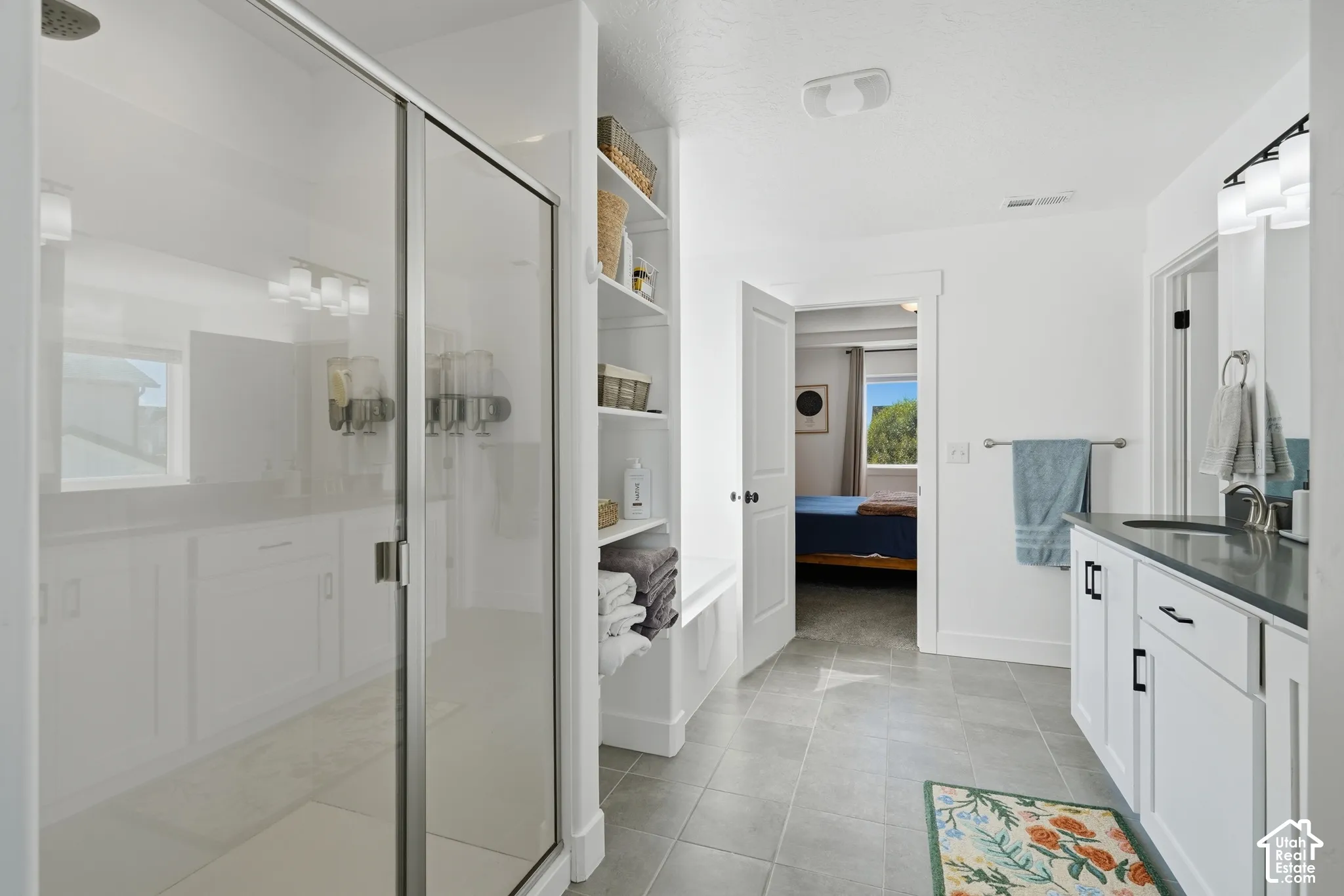 Spacious bathroom featuring a glass-enclosed shower, built-in shelving, tile flooring, and a vanity with a dark countertop