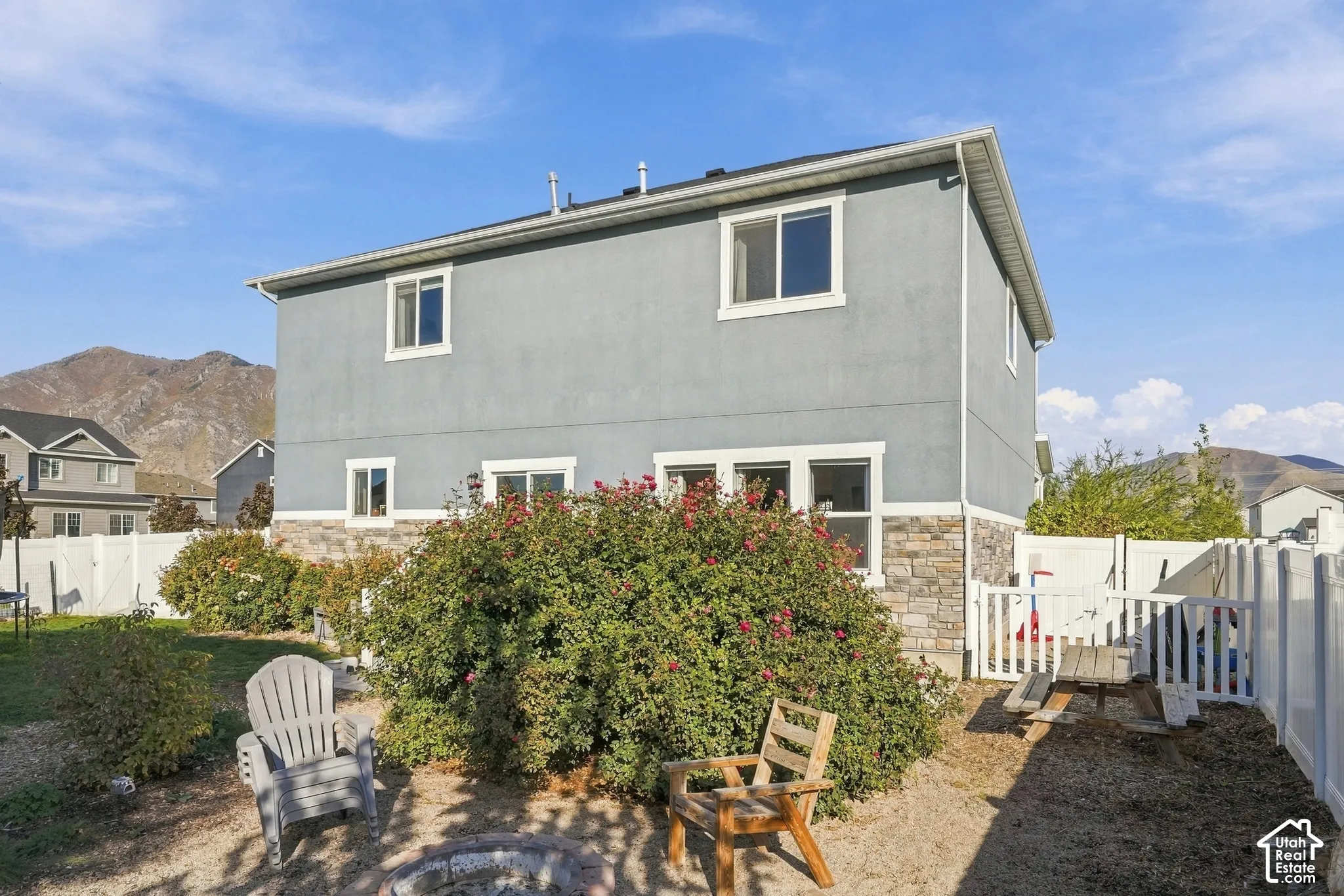 Stucco exterior with stone accent, white window trim, well-maintained landscaping, and white fencing