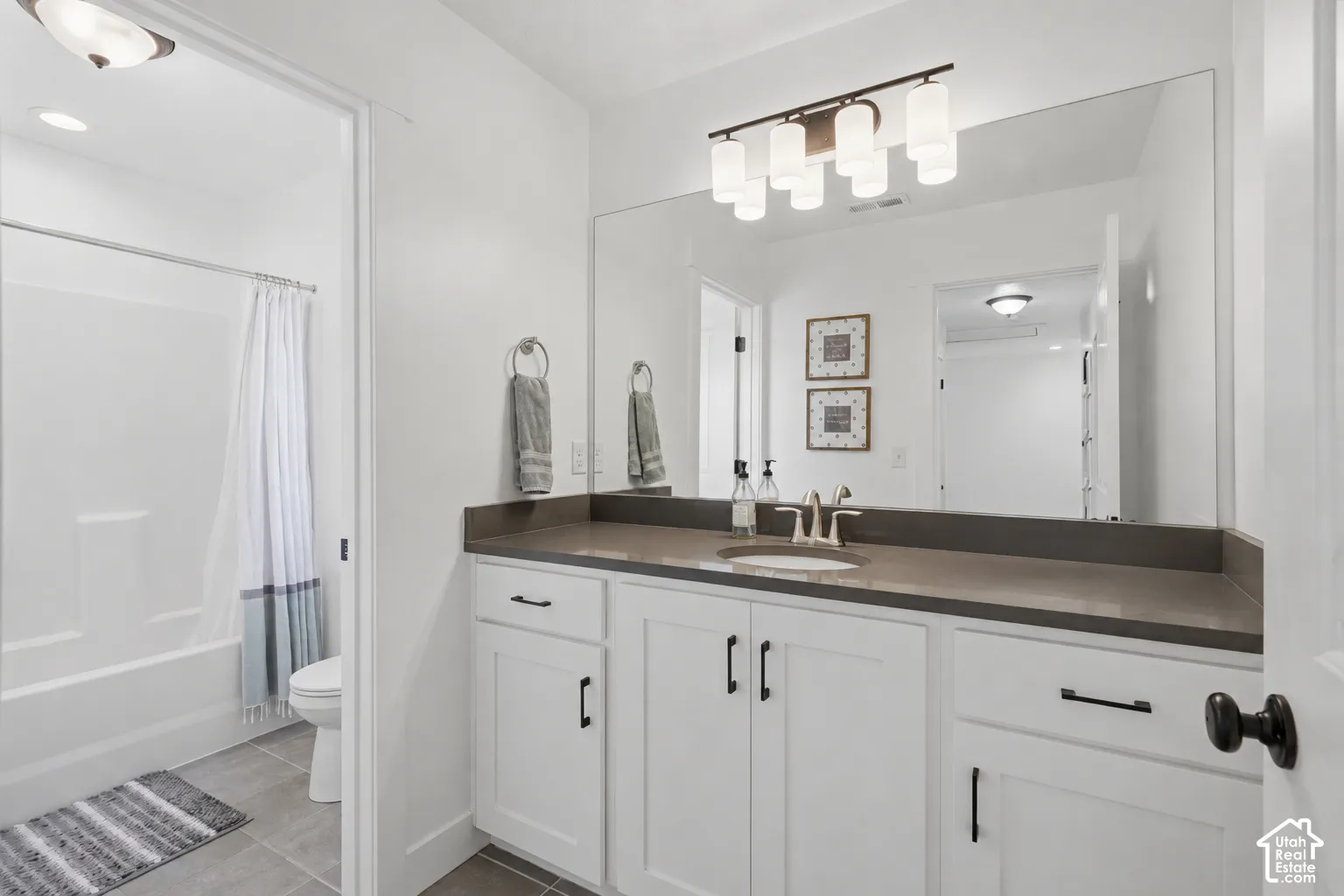 Vanity with white cabinetry and dark countertops, under-mount sink with brushed nickel faucet, large wall mirror, and a modern vanity light fixture