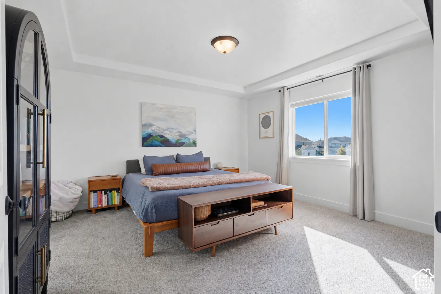 Recessed tray ceiling, neutral carpeting, window with outdoor scenery, and an arched glass-panel door