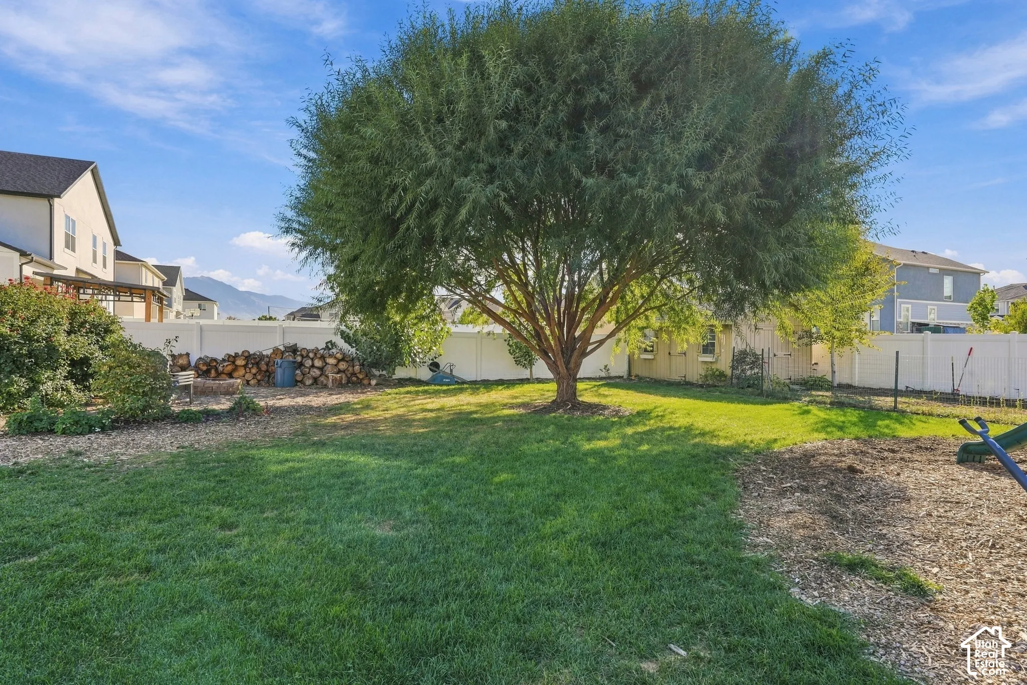 Expansive backyard featuring a mature tree, manicured lawn, and a white privacy fence