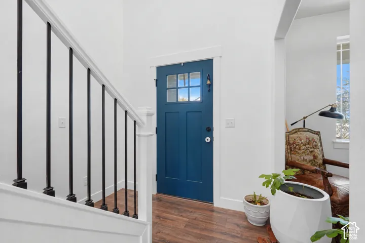 Entryway featuring a blue door with window panes, wood-finish flooring, white walls, and a staircase with white risers and black metal balusters