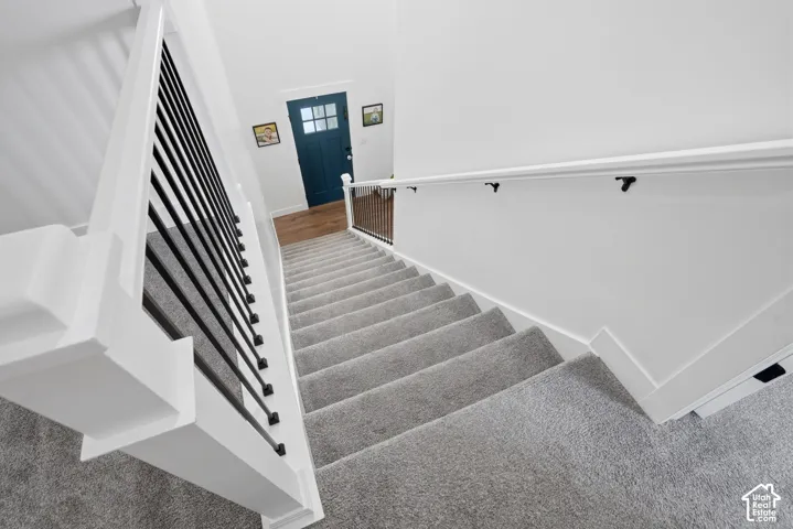 Carpeted staircase featuring a modern black metal spindle railing and a white handrail
