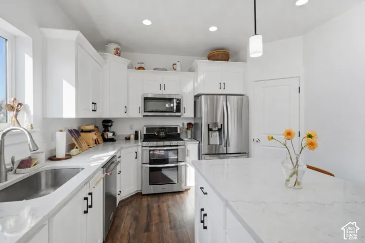 White cabinetry with black hardware, stainless steel appliances, wood-finish flooring, recessed lighting, and a kitchen island with a light-toned countertop