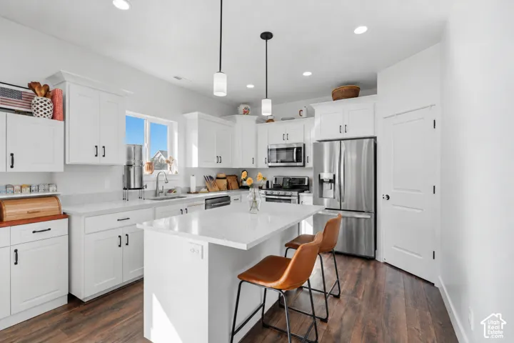 White cabinetry, wood-finish flooring, stainless steel appliances, central island with seating, and recessed and pendant lighting