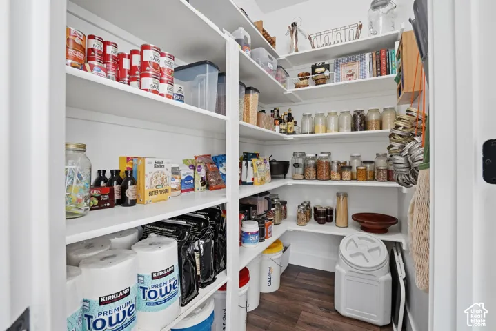 Walk-in pantry featuring white shelving, wood-finish flooring, and ample storage space