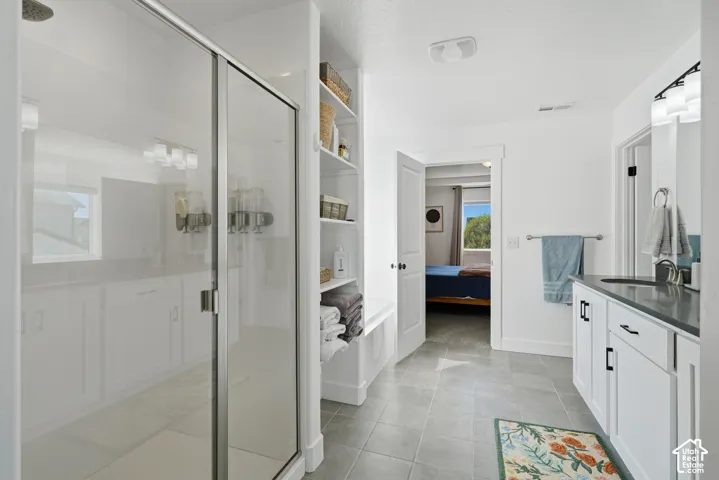 Spacious bathroom featuring a glass-enclosed shower, built-in shelving, tile flooring, and a vanity with a dark countertop