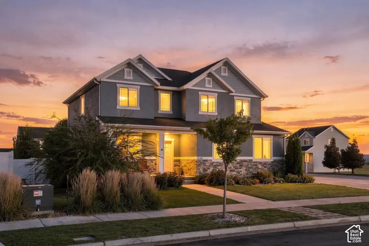 Two-story residence featuring siding and stone veneer, multiple gables, a covered porch, and a manicured lawn with established landscaping