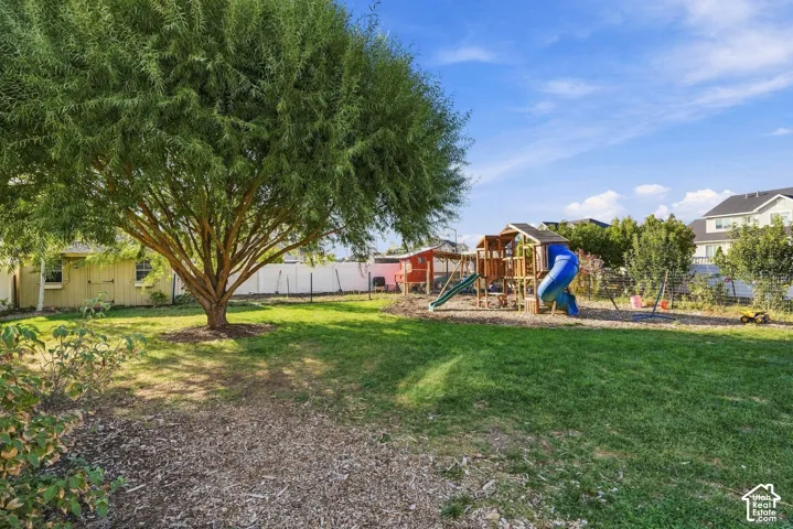 Expansive green lawn with a mature tree, bordered by a white privacy fence and an additional storage shed