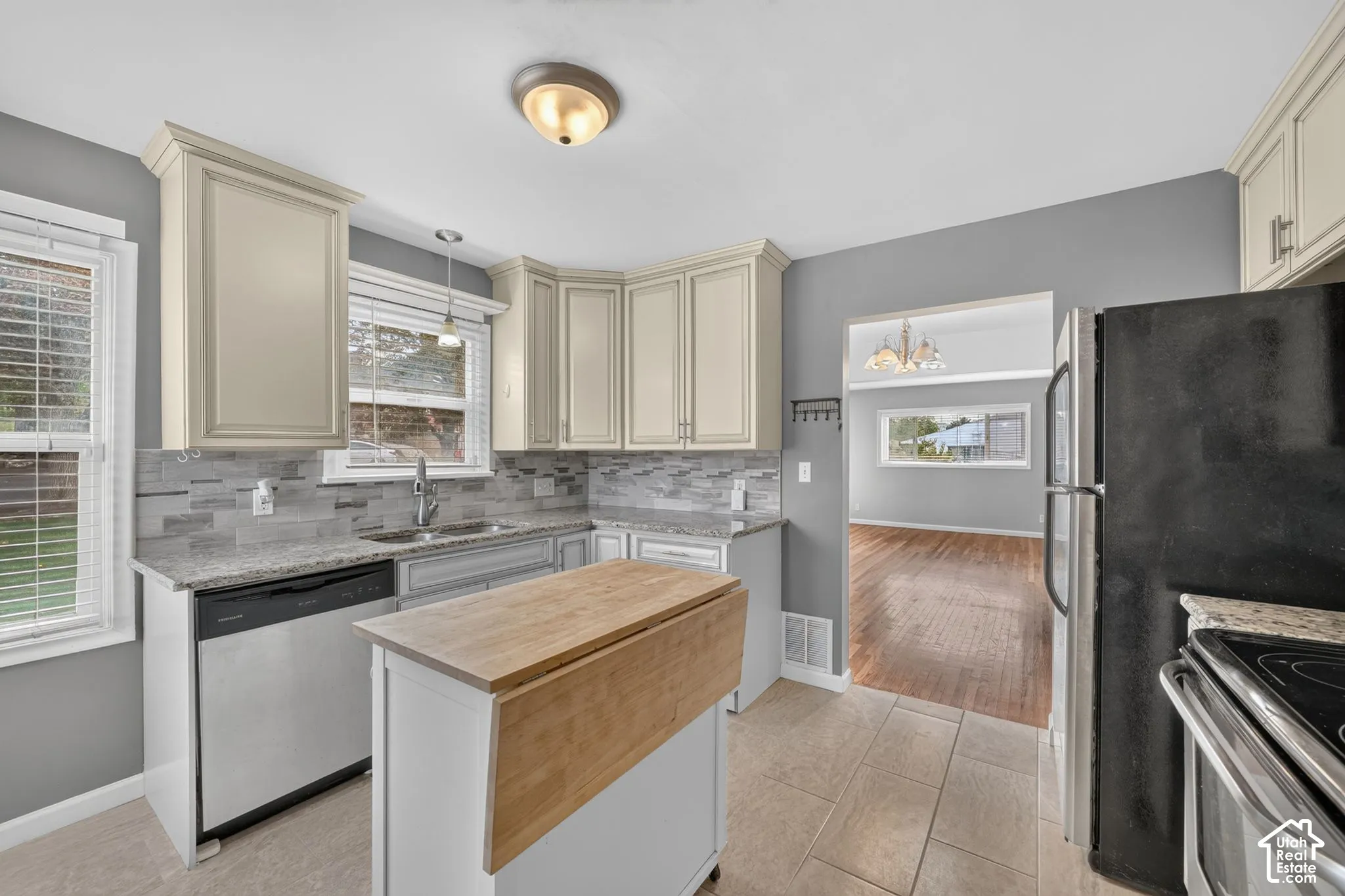 Kitchen featuring light cabinetry, granite countertops, a stainless steel dishwasher, tile flooring, and a portable island with a wood-finish top