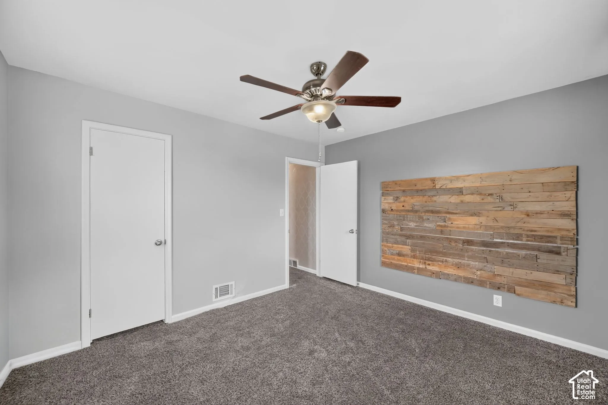 Wall-mounted wood paneling detail, textured carpet flooring, two interior doors, and a ceiling fan with integrated lighting