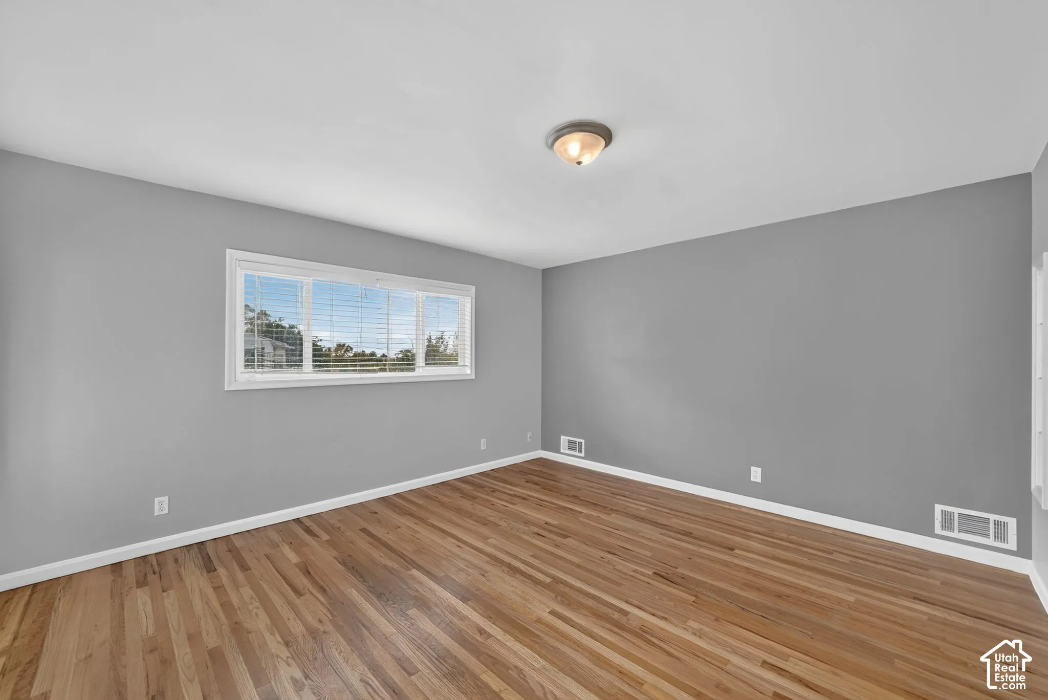 Hardwood flooring, neutral gray wall tones, ceiling-mounted light fixture, white window trim, and white baseboards