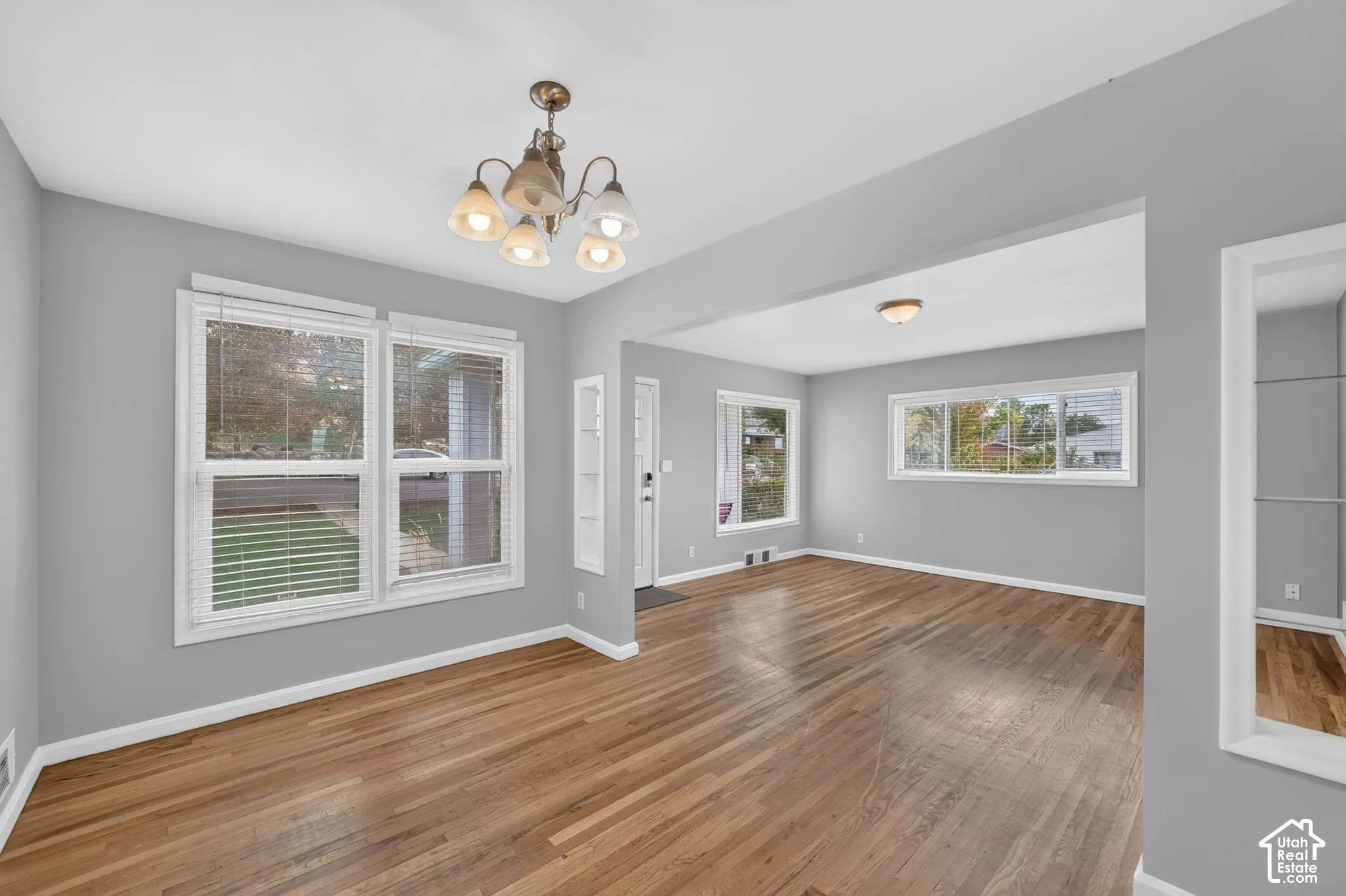 Hardwood-finish flooring, multiple windows providing ample light, a decorative chandelier, and recessed lighting