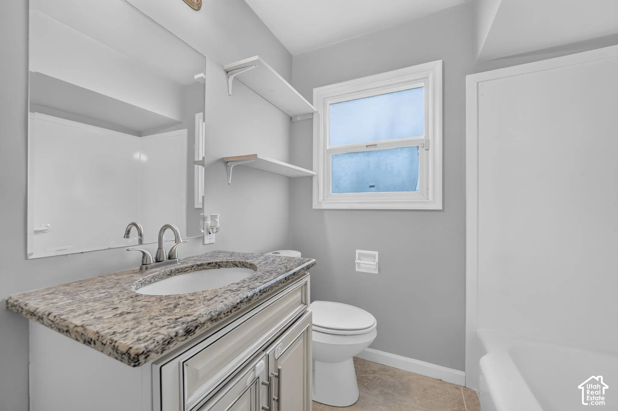 Modern bathroom featuring a granite-style countertop, white vanity, and ceramic tile flooring